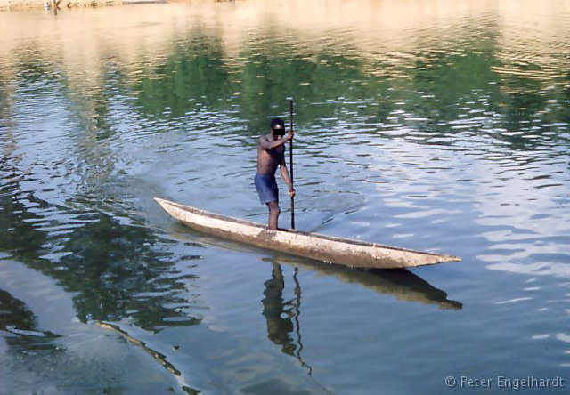 Foto einer Piroge (Einbaum), die vom Ruderer geschickt gesteuert an einem fahrenden Flußschiff auf dem Ubangi im Kongobecken anlegt.